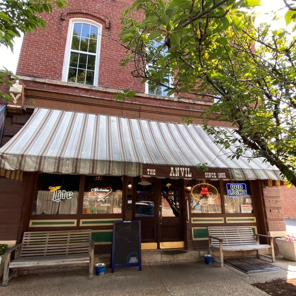 The Anvil's striped awning lettered The Anvil Since 1855, with benches and a chalkboard specials board on the sidewalk