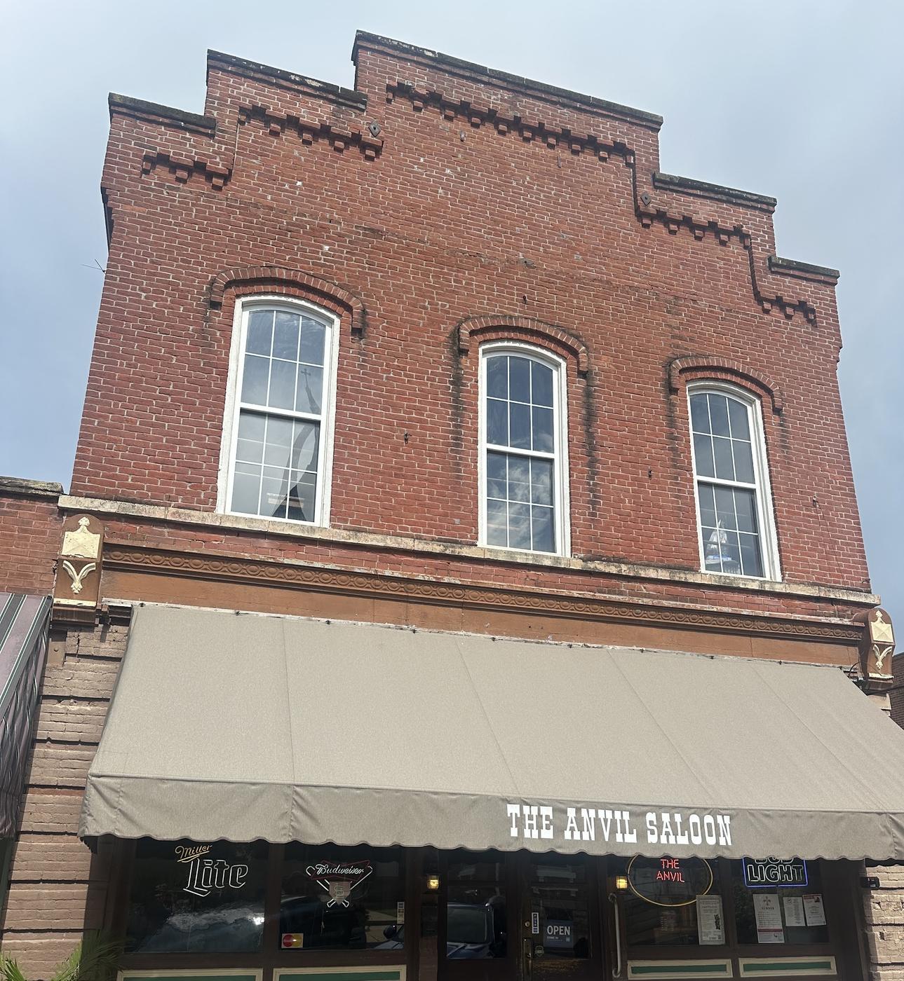 The Anvil Saloon's red brick storefront on South Third Street, with a stepped brick parapet, arched upper windows and a tan awning lettered The Anvil Saloon